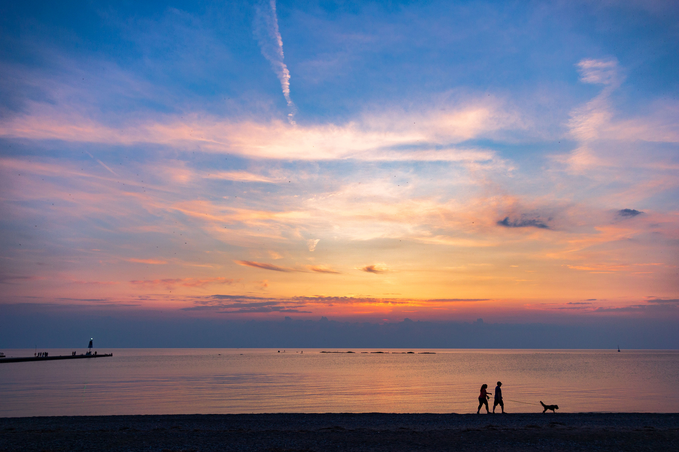 Two people walking a dog on the beach silhouetted against a sunset over Lake Huron.