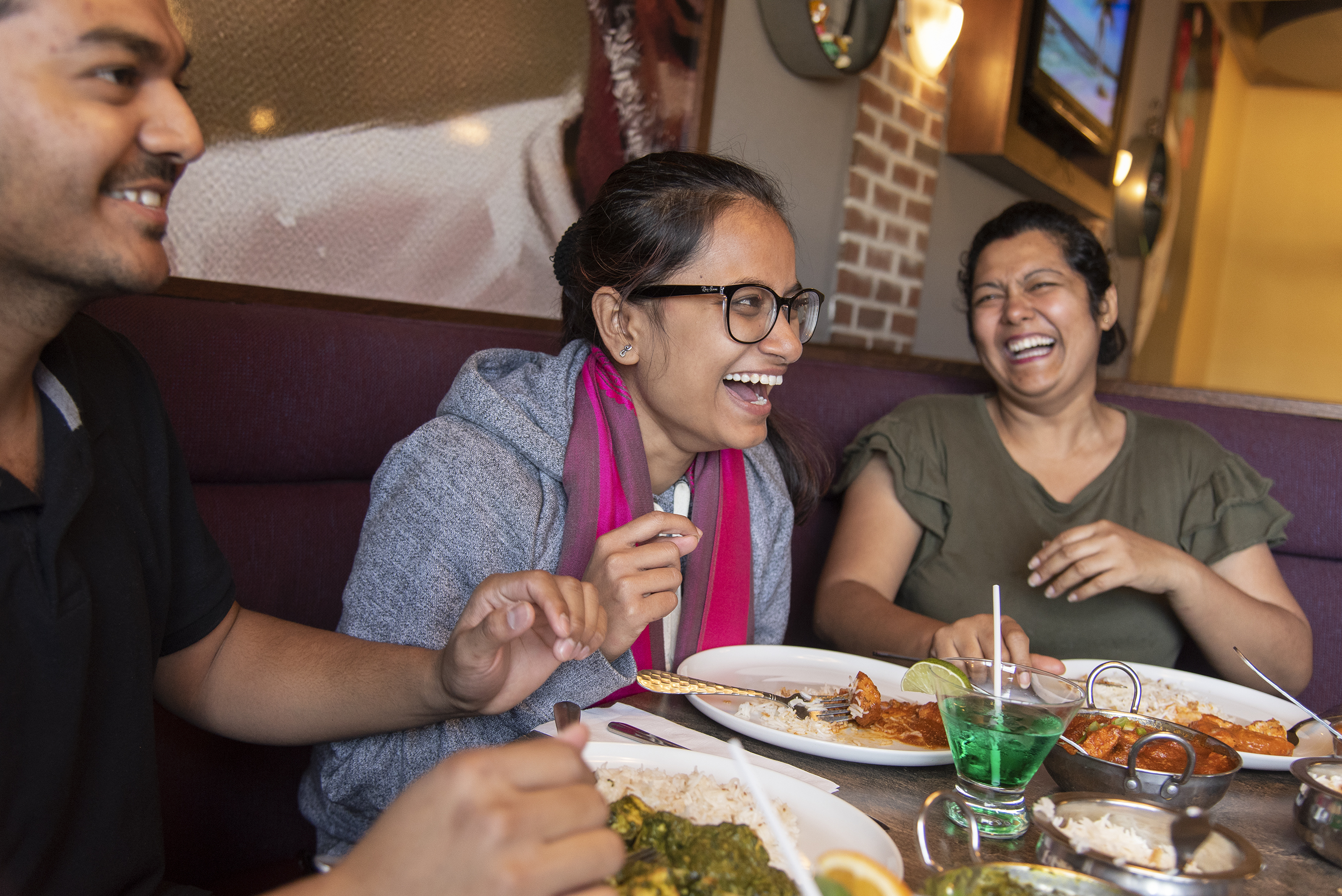 Three people laugh while enjoying a meal together.